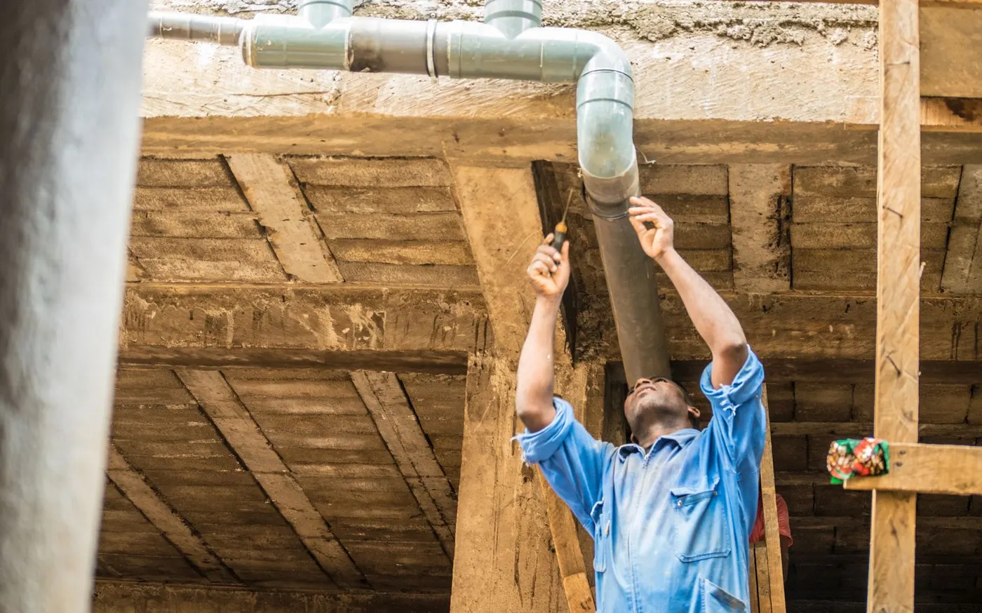 A plumber reaching up to fix a pipe