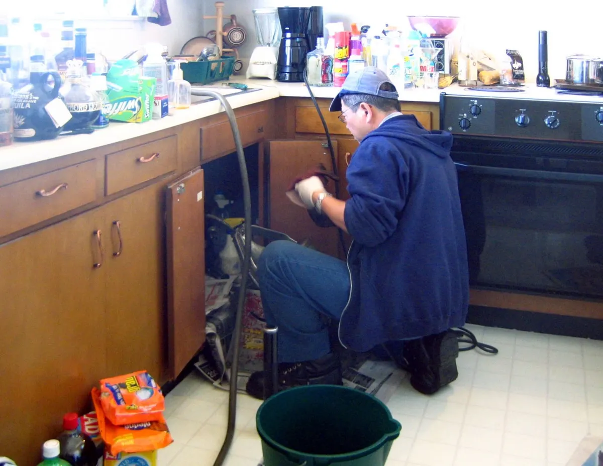 A plumber working under a kitchen sink in a real home